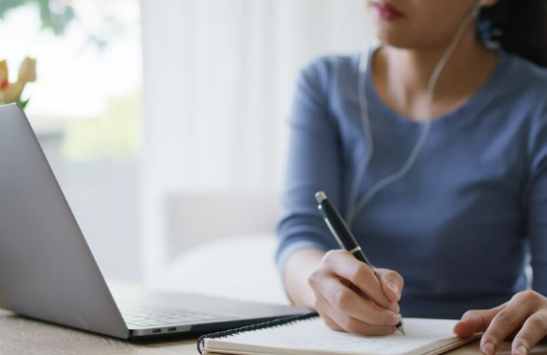 student learning something from laptop and writing on a paper