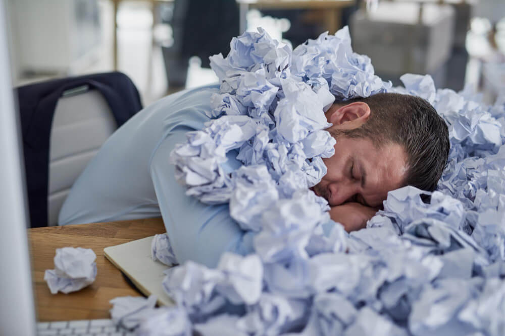 Employee buried in papers struggling with productivity and focus while working remotely on laptop